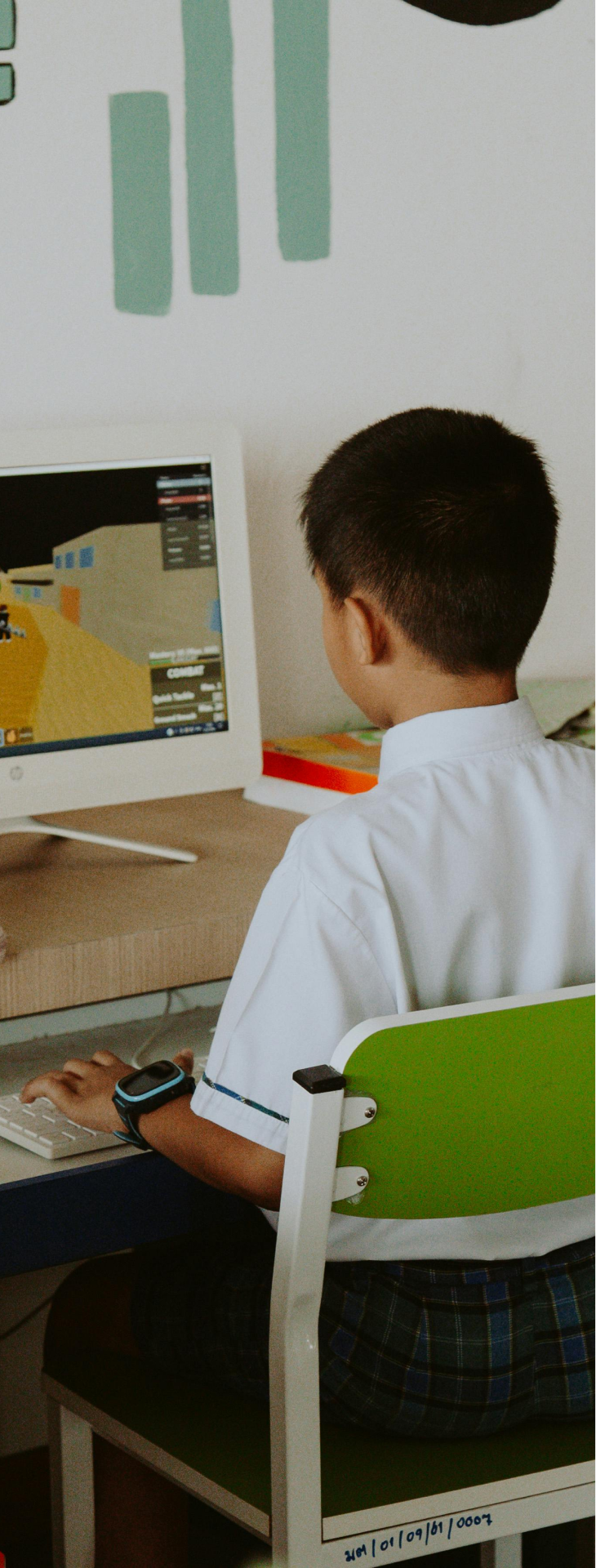 a young boy sitting on a chair with a computer on top of a desk, appearing to be engaged in online learning